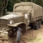 Zwei olivgrüne Militärlastwagen der US-Armee aus dem Zweiten Weltkrieg, geparkt in einem Waldgebiet.