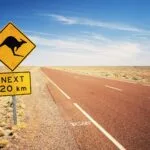 Straßenschild mit Känguru-Warnung und der Aufschrift ‚Next 20 km‘, an einer einsamen Straße in der australischen Wüste.